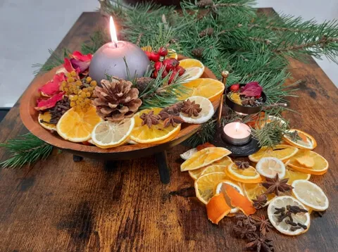 Svíčka, sušené plátky citrusů, šípky a šišky na dřevěné míse